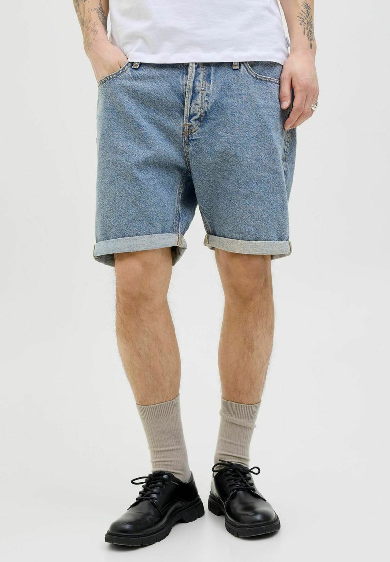 Shorts en denim de couleur bleu clair avec des ourlets retroussés, portés avec des chaussures à lacets noires et des chaussettes beiges ; dotés de poches latérales et d'une coupe classique.