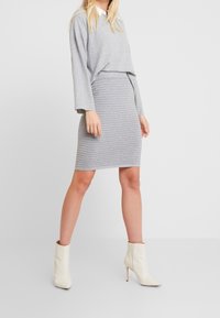 Pull gris surdimensionné avec des manches longues associé à une jupe crayon grise côtelée. Le mannequin porte des bottines beige à talons aiguilles.