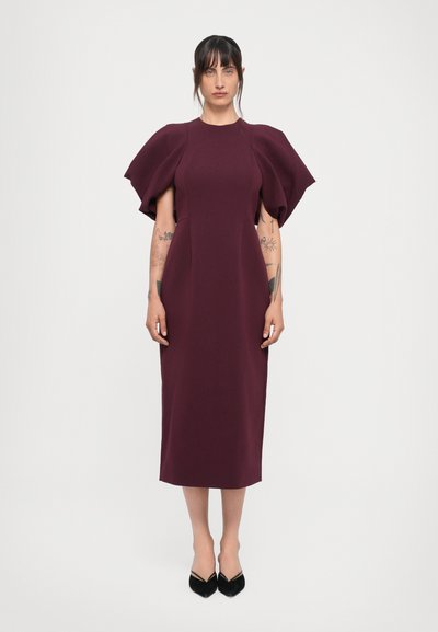 Robe midi bordeaux avec des manches bouffantes, corsage ajusté et jupe droite. Le tissu a une texture lisse, associé à des escarpins noirs à bout pointu.