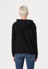 Black hooded sweatshirt with long sleeves, cotton material, relaxed fit, ribbed cuffs and hem, worn with blue jeans.