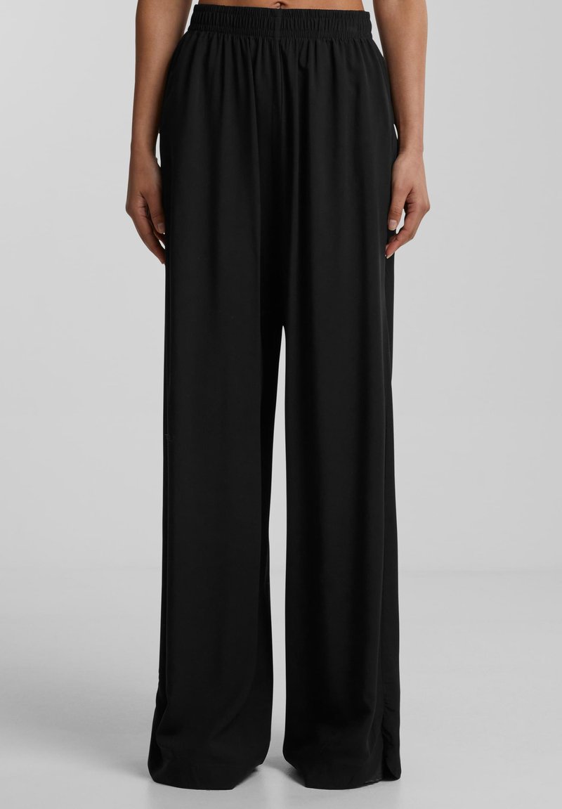 Pantaloni neri a gamba larga con vita elastica, realizzati in tessuto morbido con una texture fluida, caratterizzati da dettagli nelle cuciture laterali per un tocco di stile.