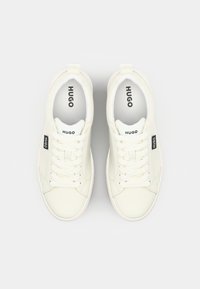 White leather sneakers with a smooth texture, featuring round toes, flat laces, and "HUGO" branding on the tongue and side.