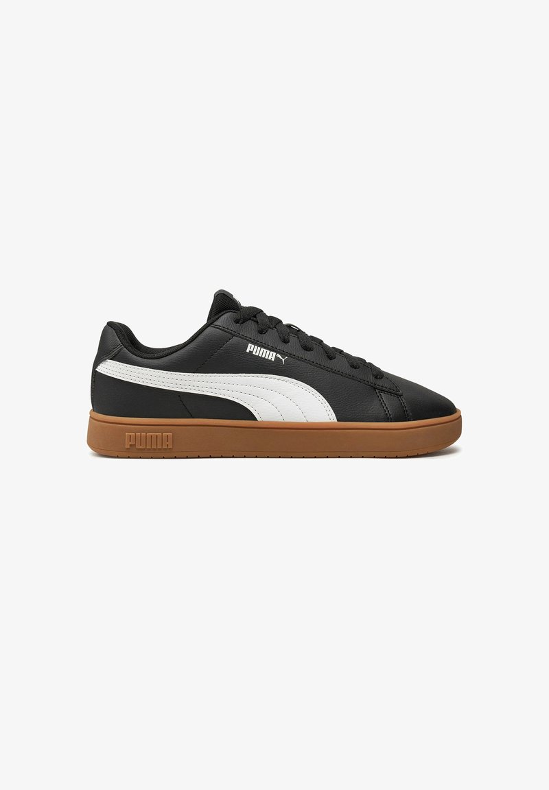 Baskets en cuir noir avec une bande Puma blanche, semelle en caoutchouc marron et design classique à lacets. Présente le logo Puma sur le côté et sur la languette.