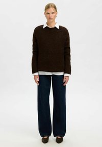 Suéter marrón y esponjoso con cuello redondo, sobre una camisa blanca con cuello, combinado con jeans de mezclilla oscuros de pierna ancha y zapatos oscuros.