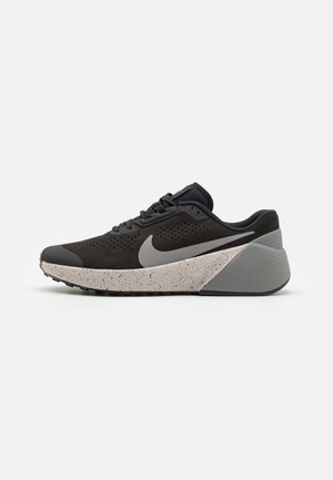 Zapatilla deportiva negra con parte superior de ante texturizado, detalles perforados, una entresuela gris moteada y una sección del talón gris sólido.
