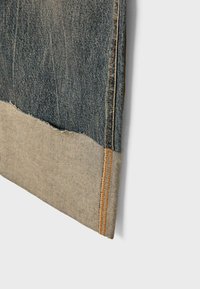 Denim tkanina s tamnoplavim gornjim dijelom i svjetlijim bež rubom. Ima rastrgane rubove i narančaste šavove duž šava.