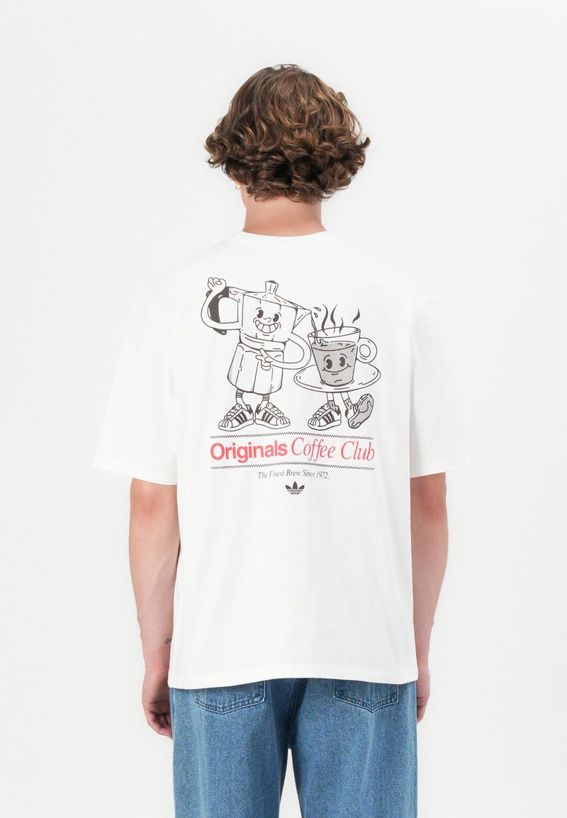 Person wearing a white T-shirt with cartoon coffee pot and cup characters and text "Originals Coffee Club" on the back.