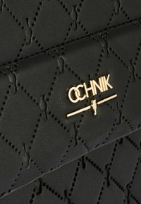 Czarna pikowana skórzana powierzchnia z diamentowym wzorem i małymi wytłoczonymi figurami, z logo marki "OCHNIK" w kolorze złotym oraz paskiem.