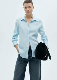 Camicia button-up blu chiaro in un tessuto morbido, con colletto e maniche lunghe. Abbinata a jeans in denim scuri e una borsa nera.