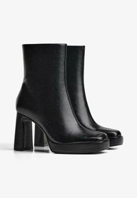 Ghete negre până la gleznă din piele cu o textură netedă, având un toc gros înalt și vârf rotunjit, proiectate cu accente decorative minime.