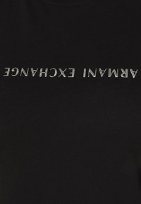 Czarna tkanina z srebrnym tekstem "ARMANI EXCHANGE" wydrukowanym do góry nogami na środku.