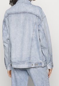 Světle modrá denimová bunda s volnějším střihem, s klasickým límcem, knoflíkovými manžetami a dvojitými švy na švech.