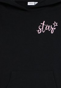 Juodas gobtuvu džemperis su priekinėmis kišenėmis, su rožinėmis blizgučiais užrašytomis žodžiais "žvaigždė" ir žvaigždutės akcentu. Minkšta, tekstūruota medžiaga.