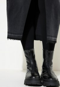 Zwarte leren laarzen met een chunky zool en een ritsdetail aan de voorkant. Gemaakt met zwarte leggings, voorzien van een versleten zoom op een donkere rok.