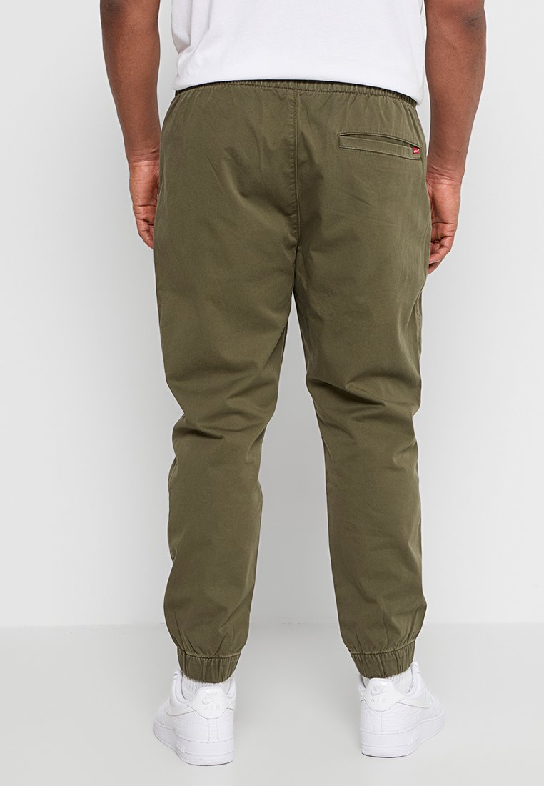 Pantaloni jogger verdi oliva con polsini elastici e una tasca posteriore. Realizzati in un tessuto leggero, presentano una vita con cordino e una minimalizzazione del marchio.
