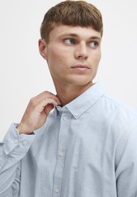 Lichtblauw overhemd met knoopsluiting, gemaakt van een fijne stof, met een puntkraag en zichtbare knoopdetails. Soepele textuur, licht getailleerd ontwerp.