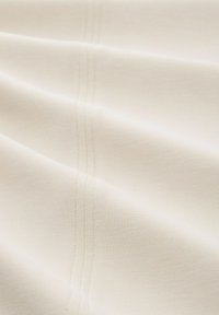 Tela color crema con una textura suave, que presenta una sutil costura horizontal. Material ligero y suave que cae con delicadeza.