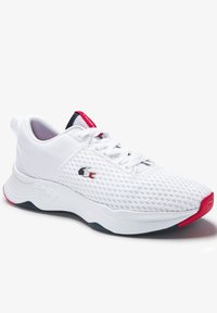 Chaussure de sport blanche avec tige en mesh, semelle texturée, accents rouges et logo Lacoste. Présente un design à lacets et un col rembourré.