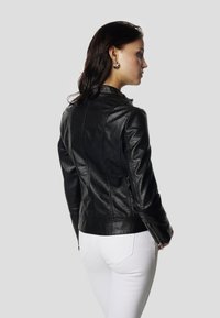 Čierna kožená bunda s priliehavým strihom, vysokým golierom a zipsami na manžetách. Má textúrovaný povrch a tvarované švy na chrbte.