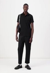 Black polo shirt with a collar, paired with black tapered trousers. Accessories include a black bag with a bold logo strap. Solid color and slim fit.
