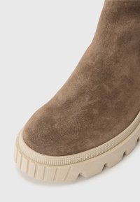 Bruine suède enkelboot met een dikke beige rubberen zool, gekenmerkt door een getextureerde rand en een afgerond te ontwerp.