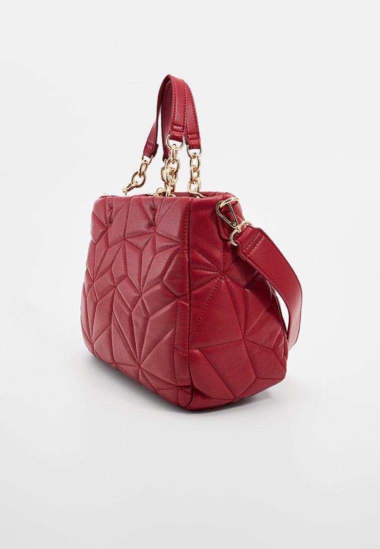 Sac à main matelassé rouge avec des coutures géométriques, poignées en chaîne dorée et bandoulière amovible sur fond uni.