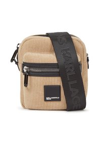 Geantă crossbody din cord din bumbac bej, cu un finisaj texturat, detalii cu fermoar negre și o curea cu logo. Formă compactă, pătrată, cu un buzunar frontal.