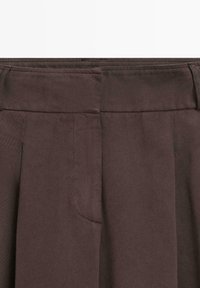Brązowe bawełniane spodnie z płaskim pasem, kieszeniami bocznymi i widocznymi fałdami, o gładkiej fakturze i klasycznym kroju.