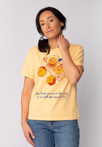 Geel katoenen t-shirt met een perzikillustratie en tekst in het blauw. Korte mouwen, ronde hals, ontspannen pasvorm, gladde textuur.