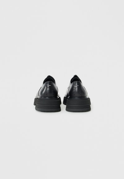 Black leather shoes with a rounded toe, thick ridged sole, and sleek design. Smooth texture with subtle vertical stitching detail at the back.