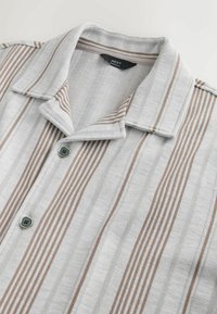 Let skjorte med krave i hvid med subtile grå og brune lodrette striber. Har en knaplukning og tekstureret stof.