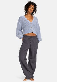 Blauwe gebreide cardigan met brede V-hals, lange mouwen en knopen. Gecombineerd met grijze cargo-broek met zijzakken en een relaxte pasvorm.
