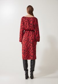 Red dress with a black abstract pattern, off-the-shoulder design, long sleeves, cinched waist, and a mid-calf length, paired with black knee-high boots.
