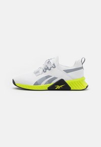 Witte sportieve schoenen met grijze strepen, gestructureerde bovenkant en een opvallende neongele hiel. Zwarte buitenzool met logo-detail.