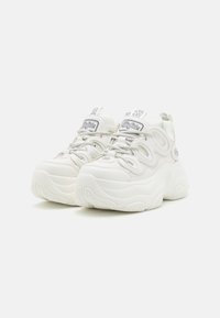 White sneakers with textured upper, chunky sole, and prominent laces. Features a logo patch on the tongue and accents on the sides.