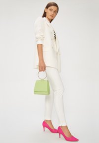 Biała marynarka z podwójnymi guzikami, białe dopasowane spodnie, jaskrawe różowe szpilki oraz mała zielona torebka z okrągłym uchwytem.