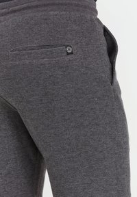 Dunkelgraue Jogginghosen aus strukturiertem Stoff, mit einer Gesäßtasche und einem kleinen schwarzen Knopfdetail sowie Seitentaschen.