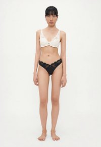 Lace bra in off-white with adjustable straps and matching black lace thong. Both feature delicate floral patterns and soft textures.