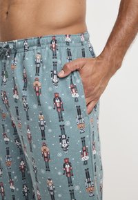 Pantalones de pijama azul claro fabricados en un tejido suave, con un diseño de cascanueces y animales, con una cinturilla elástica y bolsillos laterales.