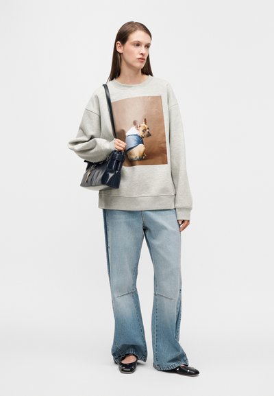 Felpa grigia con stampa di un cane, jeans denim azzurri a gamba larga, scarpe nere basse e borsa nera, su sfondo bianco.