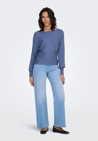 Maglione a coste azzurro chiaro con scollo ampio, abbinato a jeans a gamba larga e azzurri, e scarpe basse nere. Tessuto liscio, vestibilità casual.