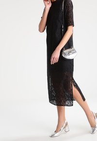 Svart spetsklänning med korta ärmar, knälång, med sidofickor. Matchad med en silverfärgad metallicaxelväska och silverklackade skor.