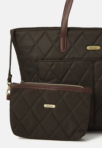 Donkerbruin gequilted tote bag en een bijpassende kleine ritszak, beide met leren details en gouden Barbour logo-plakken.