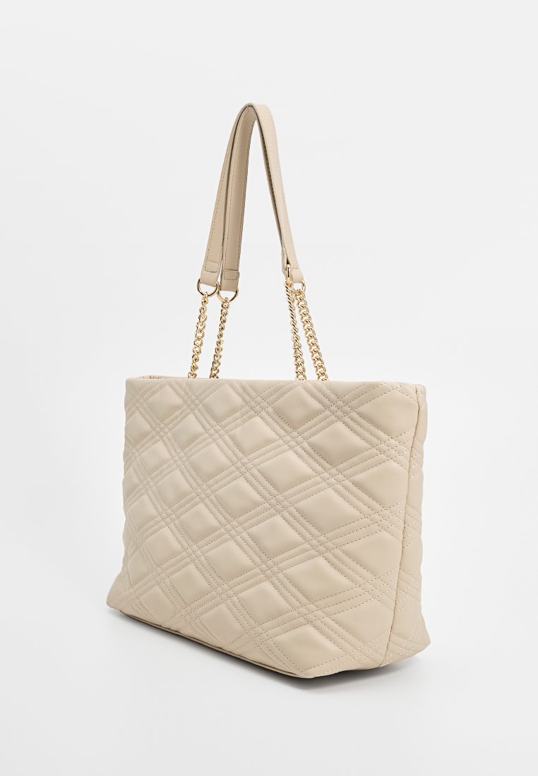 Bolso de tote acolchado beige con una textura suave, que cuenta con acentos de cadena dorada y dos asas para el hombro. Forma rectangular con una base plana.