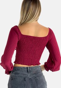 Mouwen, bordeauxkleurig top met een smock-bodice en vierkante halslijn, voorzien van elastische mouwen en een cropped zoom, gecombineerd met grijze jeans.