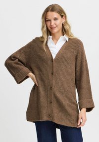 Braune, gerippte Strickjacke mit V-Ausschnitt, Knopfleiste und langen Ärmeln. Der Stoff wirkt weich und strukturiert, mit umgeschlagenen Bündchen und einer lockeren Passform.