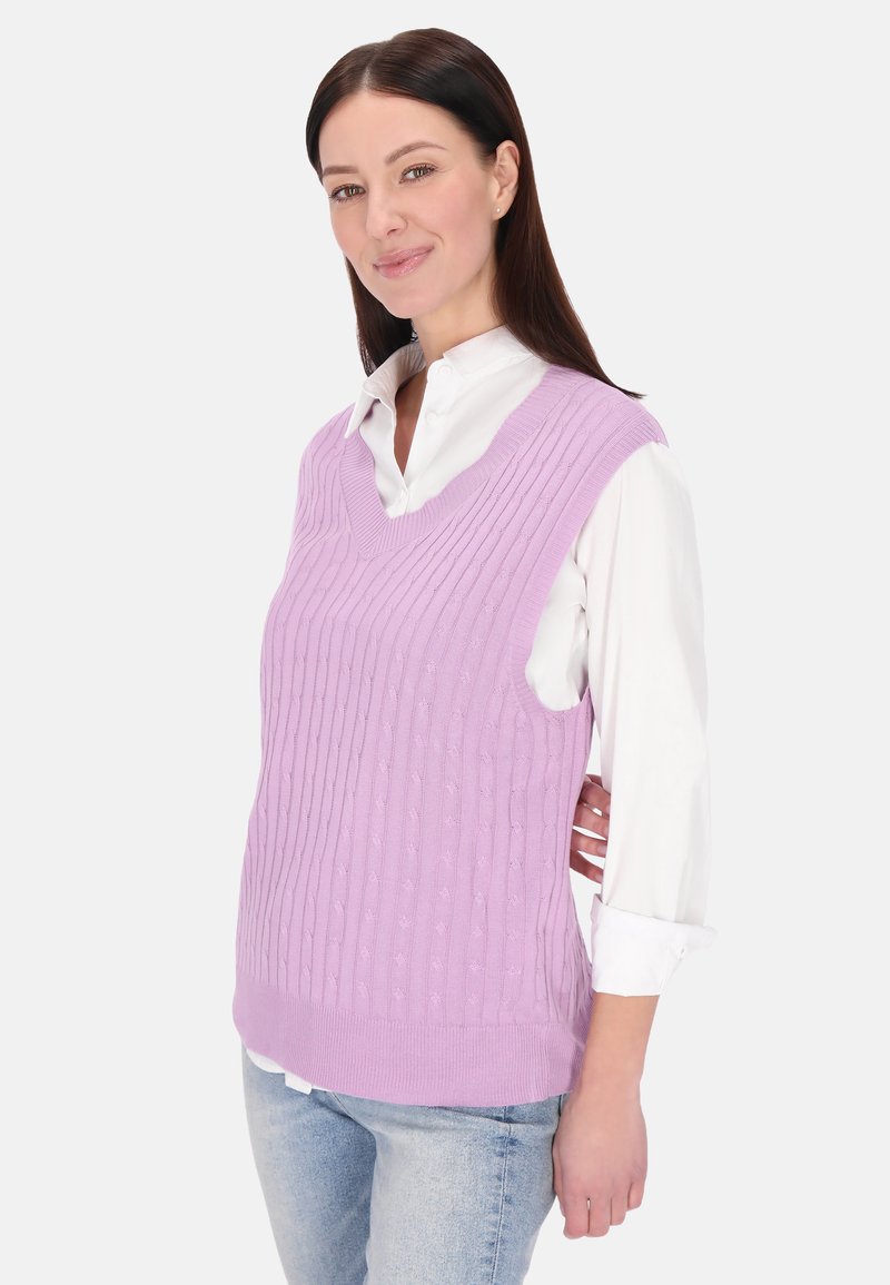 Fialová pletená vesta s výstřihem do V a žebrovanou strukturou, nošena přes bílou košili s límečkem. Má volný střih a bezrukávový design.