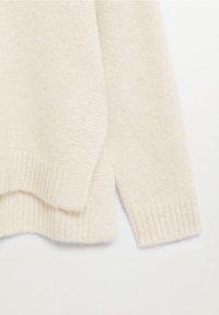 Jasno beżowy sweter z miękkim, teksturowanym splotem, ściągaczami przy mankietach oraz nieco dłuższym tylnym hemem dla luźniejszego fasonu.