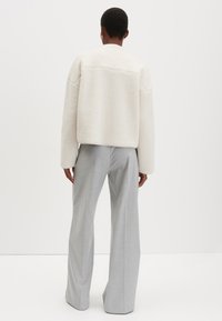 Giacca in pile bianca, testurizzata e oversize, dal taglio dritto con spalle scese, abbinata a pantaloni ampi grigio chiaro.