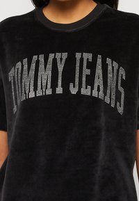 Camisa de terciopelo negro con "TOMMY JEANS" en grandes letras de brillante plateado en el pecho.